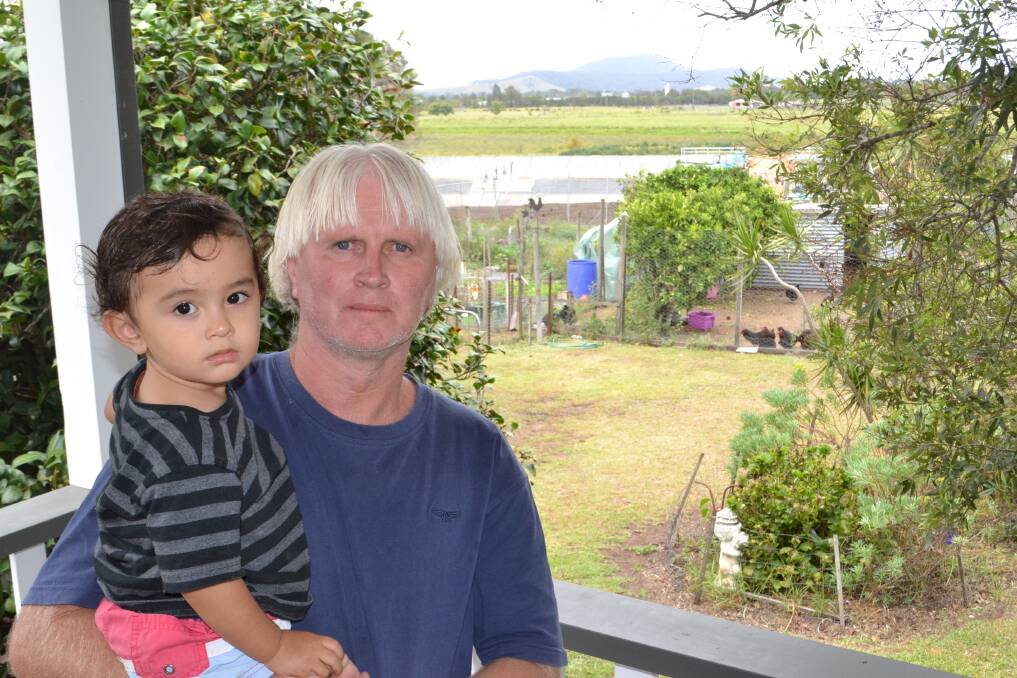 VIEW RUINED: Judd and Andrew Phillip on the deck of their property in Bomaderry. Just behind the garden is a "sludge pool" built over the past year, which will devalue their property. Picture: Rebecca Fist