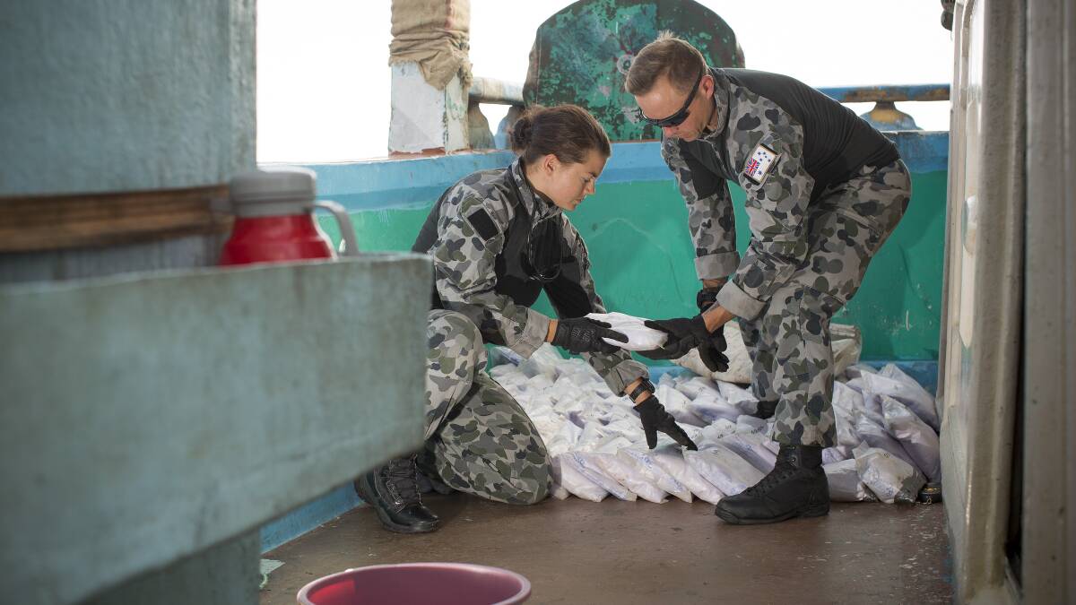 Able Seaman Boatswains Mate Stephanie Pannell (left) passes a bag a seized narcotics to Leading Seaman Physical Training Instructor James Walker during an illicit cargo seizure by HMAS Warramunga on operations in the Middle East. Photo: Tom Gibson
