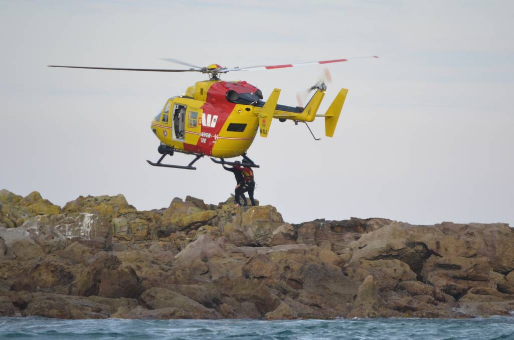 A helicopter collects a man and his daughter from a rocky outcrop off North Narrawallee Beach.
