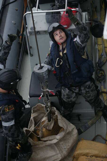HAUL: Petty Officer Matthew McDonald signals the crane operator aboard HMAS Darwin to hoist a bag filled with illegal narcotics seized from a skiff in the Arabian Sea. 