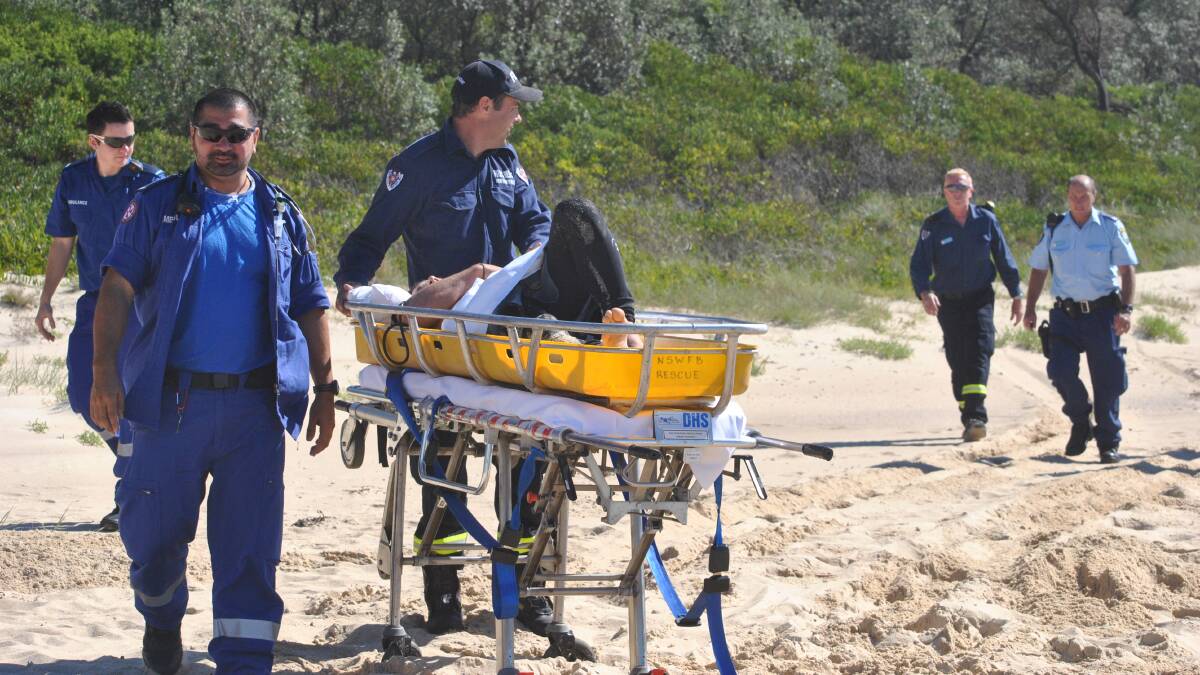 INJURED: Paramedics, police and NSW Fire and Rescue personnel attend to injured bodyboarder John Wolfson after pushing a bogged ambulance out of soft sand.
