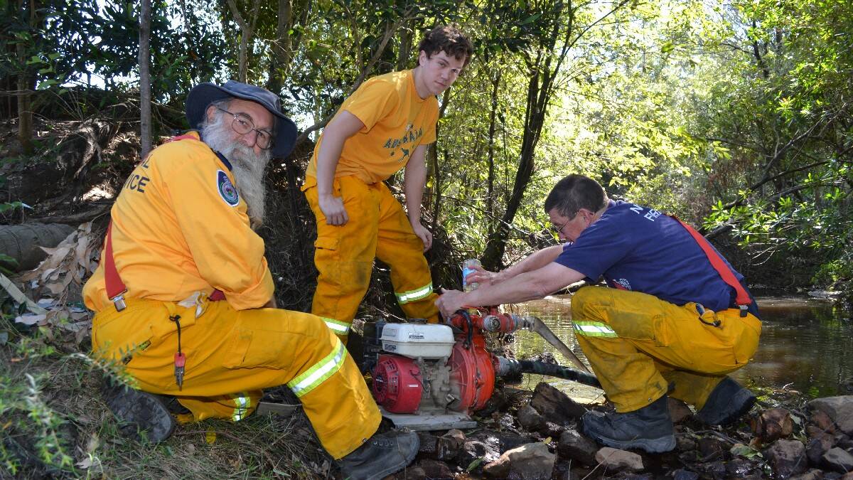 Firefighters from Culburra Beach brigade, Bob, Burton, Matt Crowe and Brian Perry use a mobile pump in a creek to refill their tanker on the Wandandian fire ground.