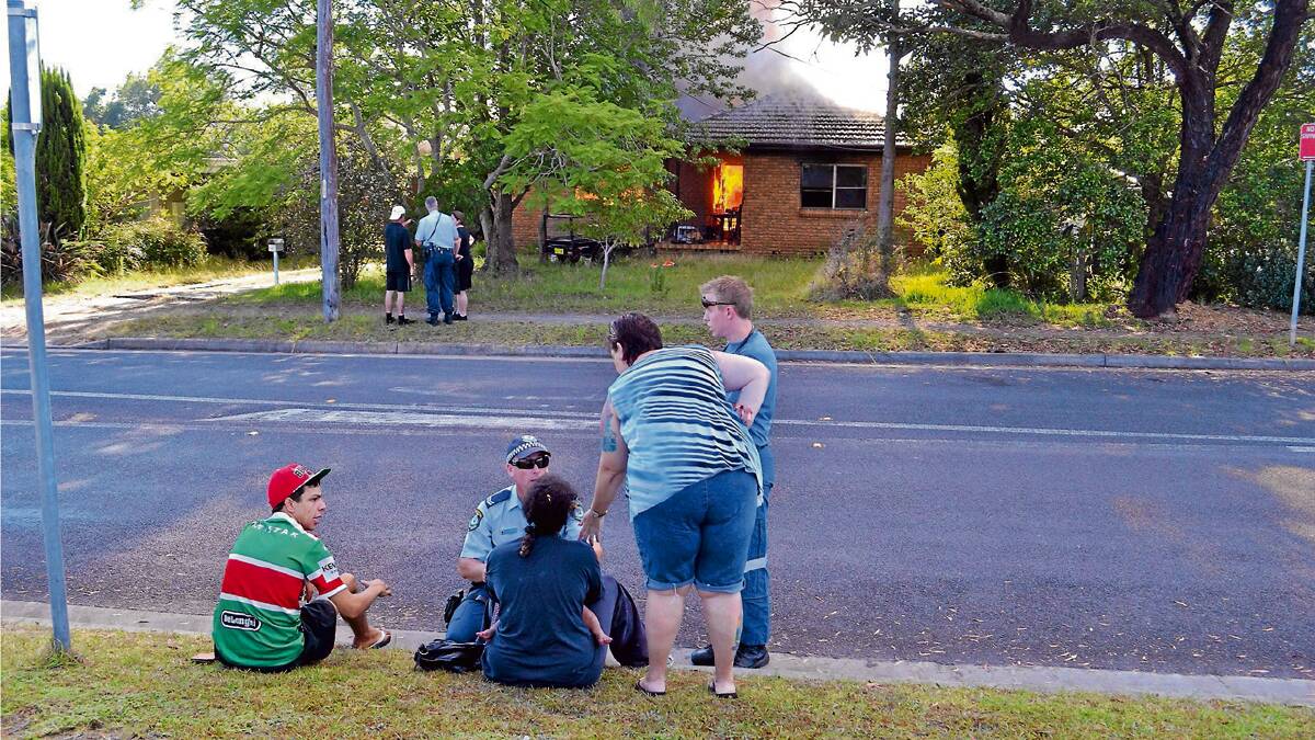 CLOSE CALL: A mother and her child, who was rescued from the fire at North Nowra on Thursday morning, are comforted by police, ambulance personnel and residents as their home burns.