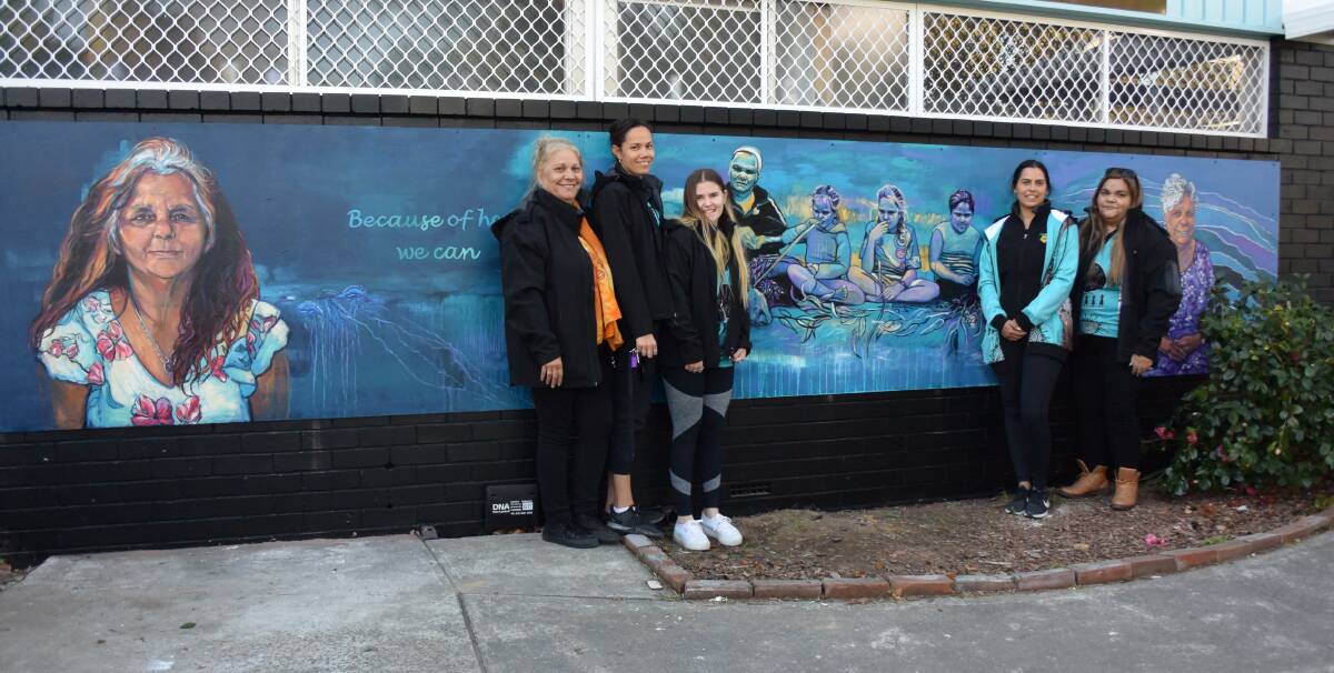 BEACUSE OF HER, WE CAN: Lynn Wellington, Hayley Longbottom, Kalinda Wills, Emma Ardler and Cleone Wellington with the mural of Aunty Marie Stewart, Aunty June Grundy and Aunty Wendy Brown.