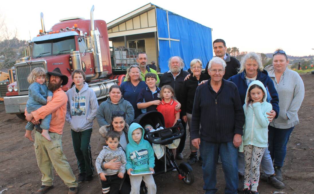 FAMILY IS WHAT'S IMPORTANT: Ron Corby (third from right) stands at his block in Cobargo surrounded by four generations of his family as his new house is delivered by truck on Tuesday. Picture: Albert McKnight 