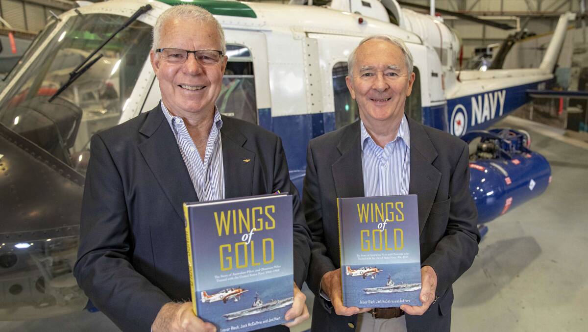 HISTORY: Former naval aviators, Jed Hart (left) and Commodore Jack McCaffrie (Rtd) hold their book 'Wings of Gold' in front of a UH-1 Iroquois helicopter at the Fleet Air Arm Museum at HMAS Albatross. Photo: Cameron Martin