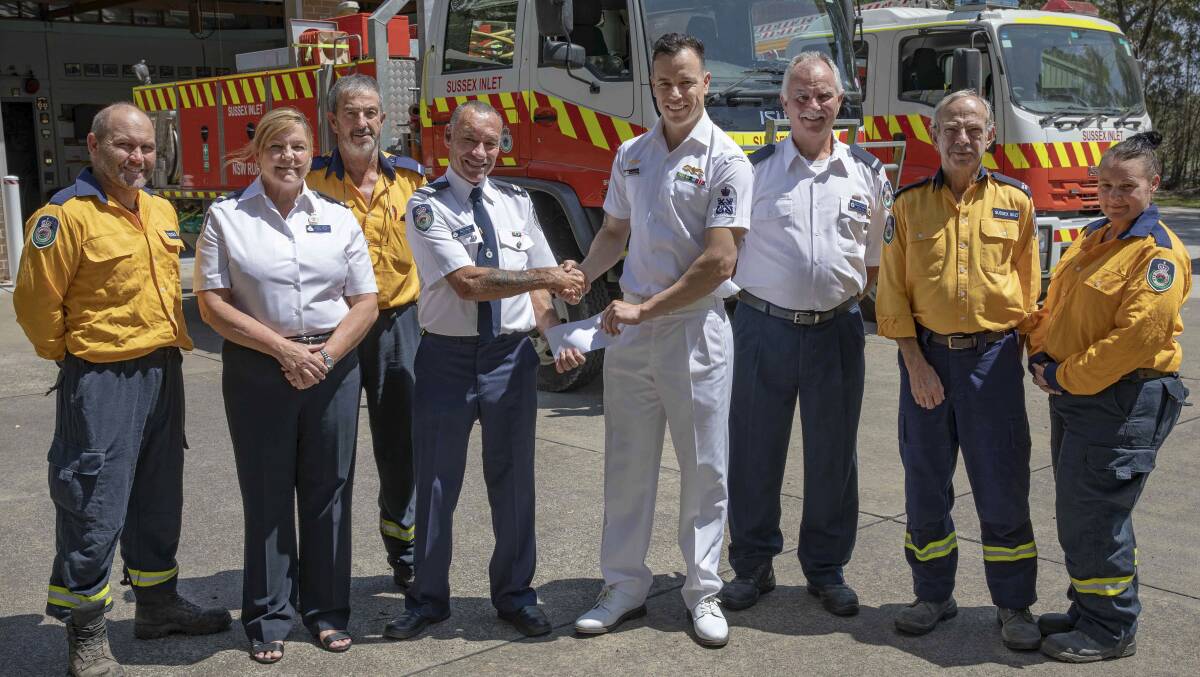 DONATION: Petty Officer Aircrewman Liam 'Emu' Carruthers hands Sussex Inlet Rural Fire Brigade deputy captain Garry Brown, a cheque for $9000, the proceeds of the charity auction he organised with (from left) Terry Davies, Debbie Simpson, Wally Cook, Garry Brown, Manfred Simpson, Terry Davies, Jim Denchem and Mandy Cropper. Photo: Cameron Martin