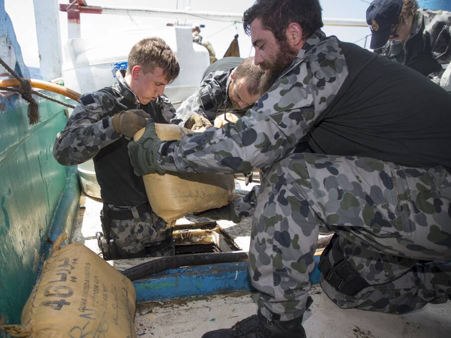 Able Seaman Electronic Warfare Justin Springer and Leading Seaman Marine Technician Daniel Colliver remove sacks containing suspected narcotics during a search of a suspicious dhow by HMAS Ballarat's boarding party. Photo: Bradley Darvill