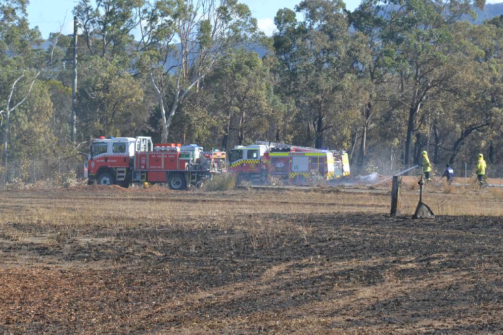 Fire and Rescue NSW and NSW RFS members work to extinguish a smoldering area of mulch in the scorched grass area behind the Bomaderry Motor Inn.
