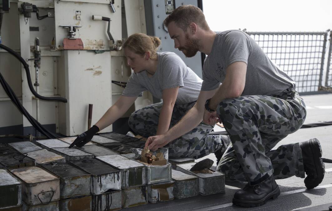Lieutenant Megan Ryan and Lieutenant Morgan Pierce check the markings on boxed ammunition seized during a boarding of a dhow by HMAS Ballarat. Photo: Bradley Darvill
