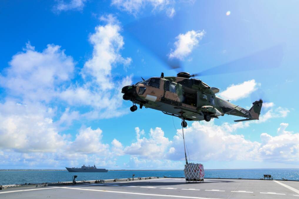 REPLENISHMENT: A Nowra-based Royal Australian Navy MRH-90 Taipan helicopter from 808 Squadron, embarked on HMAS Adelaide during Operation Tonga Assist 2022 conducts a vertical replenishment of stores from HMAS Supply. Photo: Rye Huckel