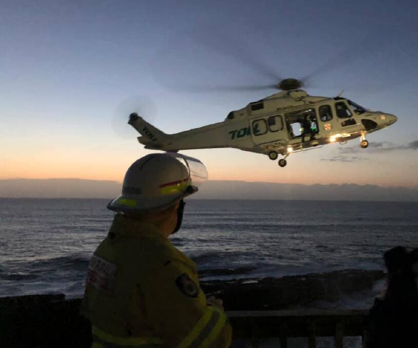 A Culburra Beach Rural Fire Service member watches on as the Toll NSW Ambulance Rescue Helicopter airlifts the injured woman from Penguin Head. Photo: Darryn Jose