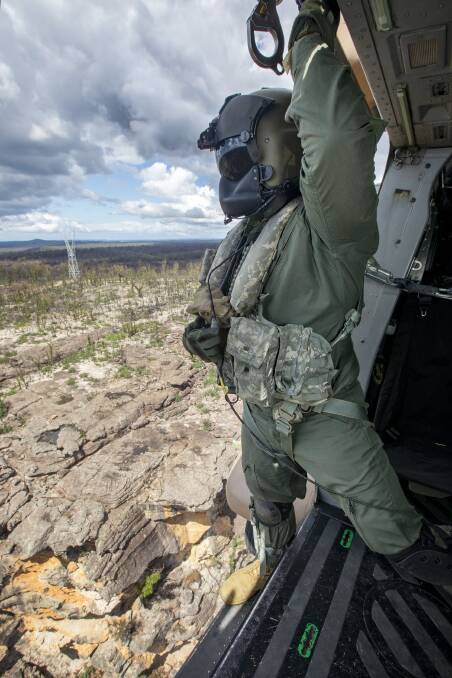 Leading Seaman Aircrewman Bradley Thomas of 808 Squadron surveying a fire ravaged Moreton National Park to find a safe landing spot to distribute food for the local wildlife. Photo: Cameron Martin
