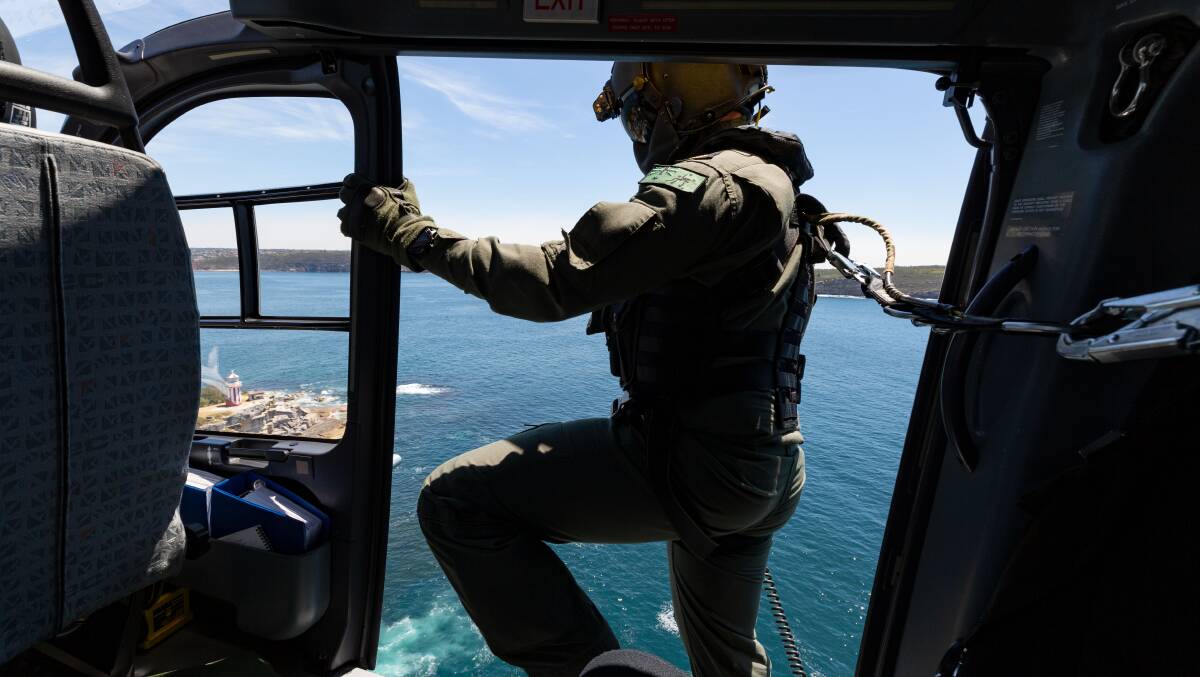 RAN aircrewman Leading Seaman Sean Coxell keeps watch for obstructions as a 723 Squadron EC-135T2+ helicopter prepares to land at HMAS Watson, Sydney. Photo: Shane Cameron