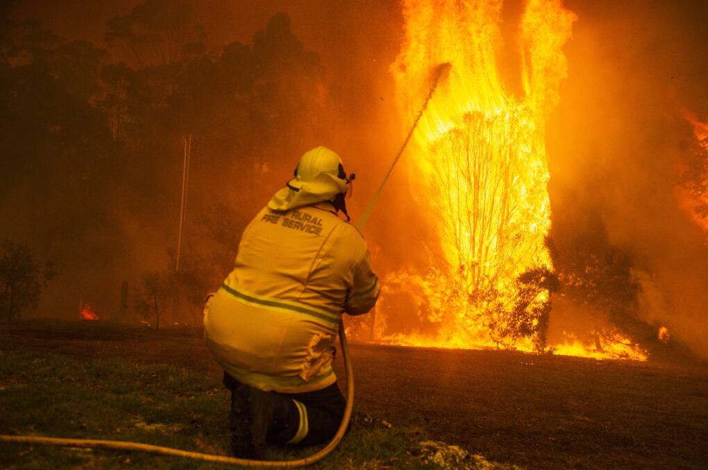 A firefighter from the Wreck Bay Rural Fire Service crew protects a property on Jindelara Creek Road from the Currowan fire. Picture: Dion Georgopoulos