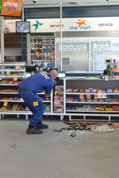 SMASHED UP: A forensic services officer photographs the crime scene at the Star Mart Caltex Service Station at South Nowra after a robbery on Thursday.