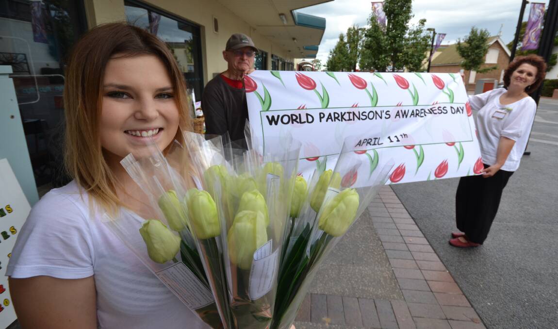 SUPPORT: Mikayla Foster from North Nowra with a tulip for Australia’s first Parkinson’s disease awareness day. Behind her are members of the Shoalhaven Shufflers, Greig Nichols and Jo Szczepanowski, holding the first Tulip Day banner.