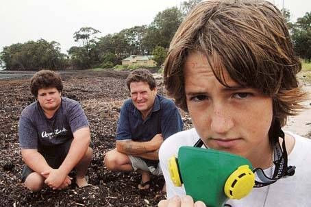 WEED WORRIES: Quinten Lay looks for protection from the stench coming from rotting seaweed on Callala Bay, while brother Samuel and dad John take a closer look at the huge pile of weed.